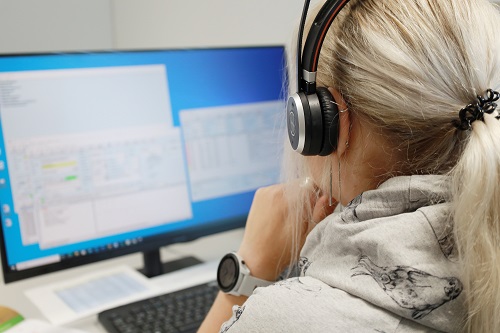 Henkilö kuulokkeet päässä katselee tietokoneen näyttöä..